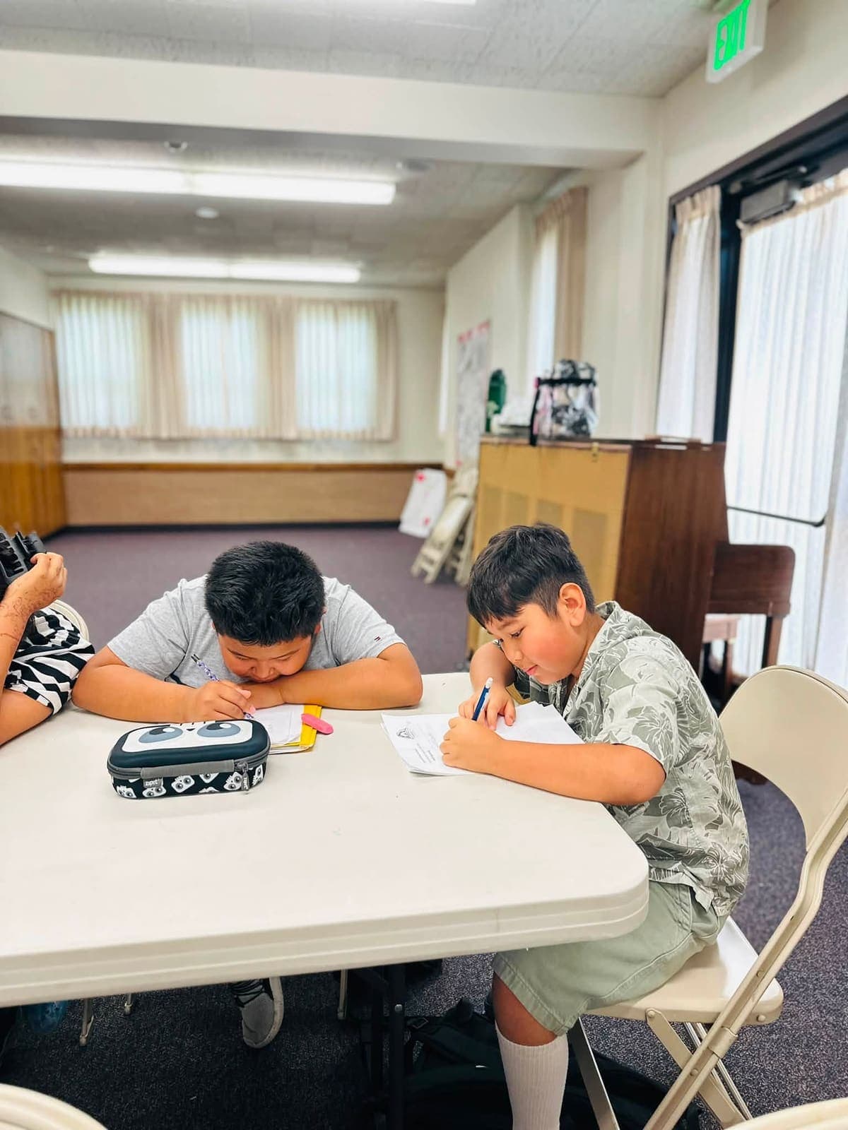 Two boys working through Nepali writing exercises at a folding table